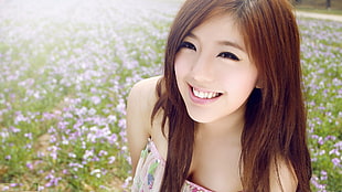 woman in pink and green floral strapless top taking picture with field of purple-and-white petaled flower field smiling during daytime